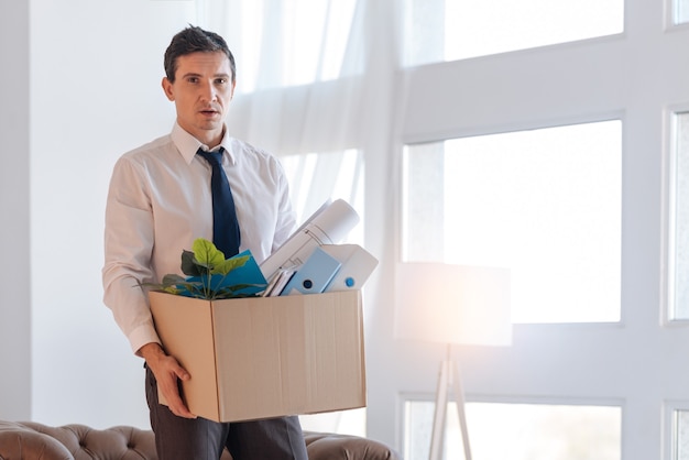 Boîte pleine. Triste homme déçu fatigué portant une grosse boîte lourde avec des objets personnels tout en rentrant à la maison de mauvaise humeur après avoir perdu son emploi