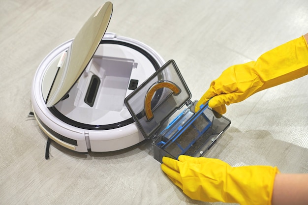 Boîte de rangement de la poussière de l'aspirateur robot dans les mains gantées des femmes.