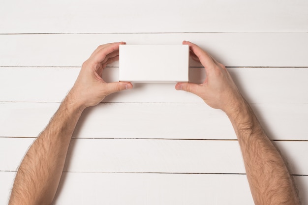 Boîte rectangulaire blanche entre des mains masculines. Vue de dessus.