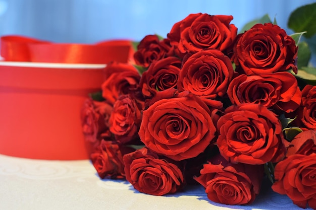 Boîte ronde rouge attachée avec un ruban rouge. Bouquet de roses écarlates à proximité. Fête des mères, Saint Valentin.