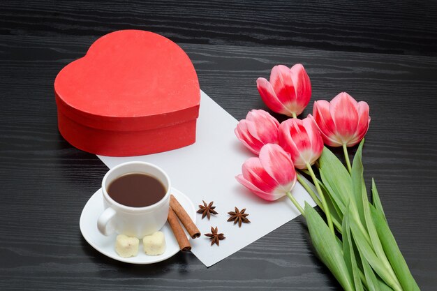 Boîte rouge en forme de coeur, tulipes roses, feuille grise et une tasse à café