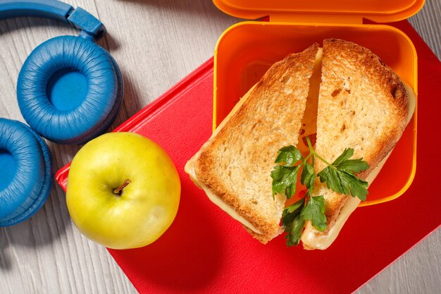 Boîte à sandwich jaune avec des tranches de pain grillées au fromage et des écouteurs de pomme verte au persil vert