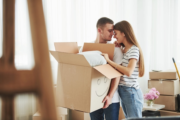 Boîte avec un sourire peint dessus. Joyeux jeune couple dans leur nouvel appartement. Conception du déménagement.