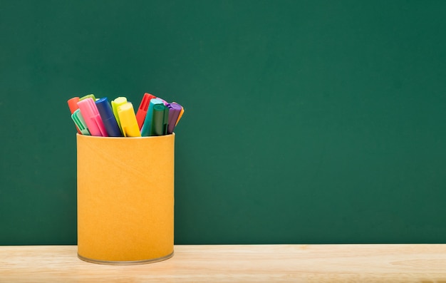 Boîte de stylo coloré sur la table avec un mur de tableau vert