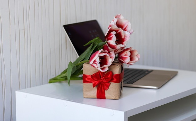 Une boîte de tulipes est posée sur un bureau à côté d'un ordinateur portable.