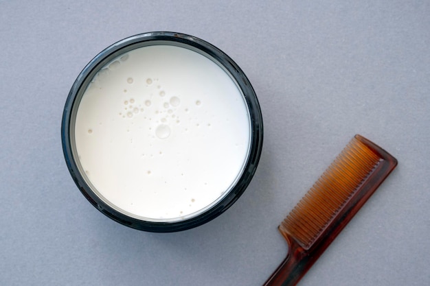 Boîte en verre avec crème de mousse de cire blanche et brosse à cheveux en plastique sur surface grise