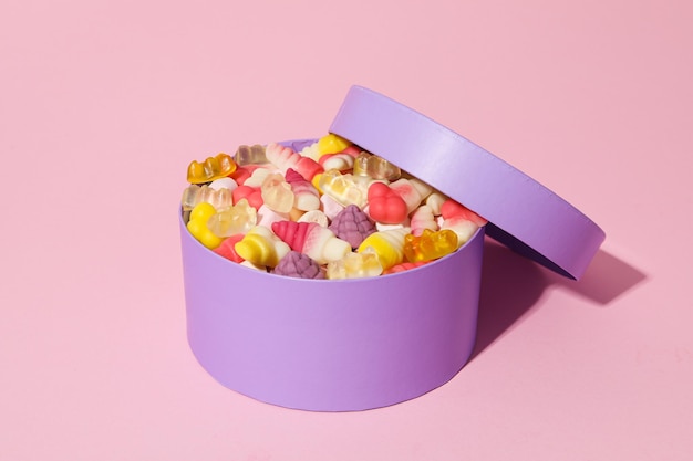 Boîte violette avec des bonbons à la gelée sur fond rose