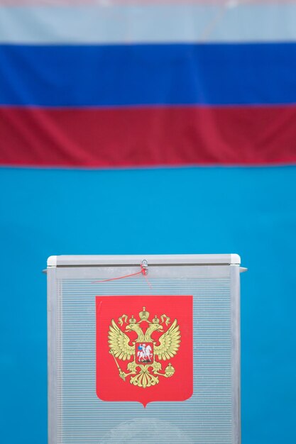 Photo boîte de vote pour l'élection présidentielle avec bulletins de vote devant le drapeau russe