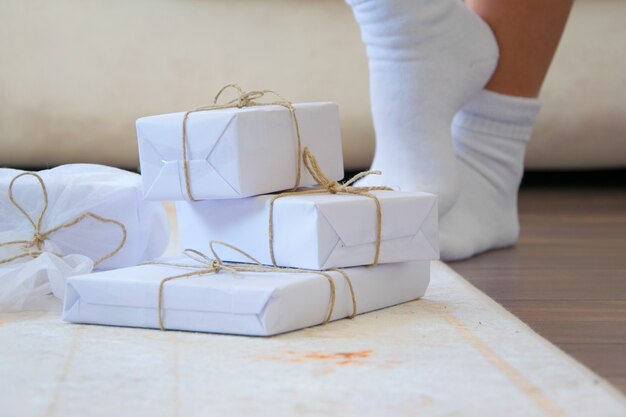 Photo boîtes-cadeaux artisanales blanches élégantes sur le tapis de sol en bois, une personne avec des chaussettes blanches se tient en arrière-plan