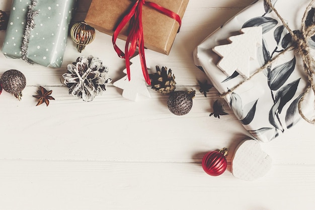 Photo boîtes cadeaux emballées avec ornements cônes de pin anis sur fond en bois blanc vue de dessus espace pour texte noël plat poser carte de voeux saisonnière joyeuses fêtes