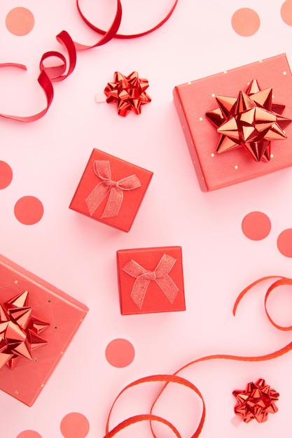 Boîtes à cadeaux rouges avec des nœuds, des rubans et des confettis sur fond rose