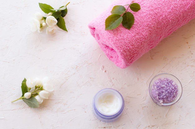 Boîtes avec du sel de mer et de la crème pour la peau, une serviette et des fleurs de jasmin sur une surface blanche