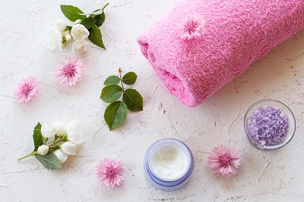 Boîtes avec du sel de mer et une serviette de crème pour la peau et des fleurs de jasmin sur fond blanc