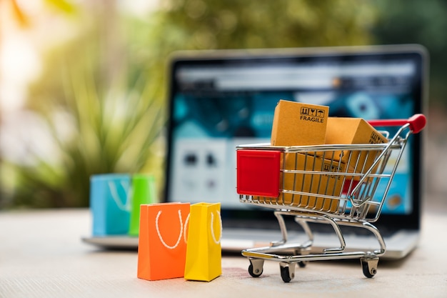 Boîtes d'emballage de produit dans le panier avec sac à provisions et ordinateur portable