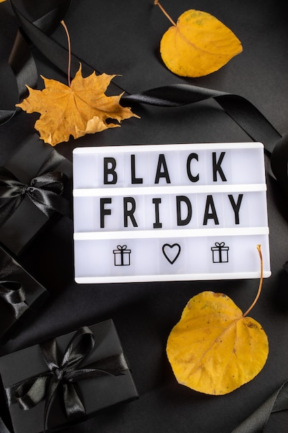 Photo boîtes enveloppées de noir boîte à lumière avec lettres black friday feuilles d'automne jaunes sur fond noir