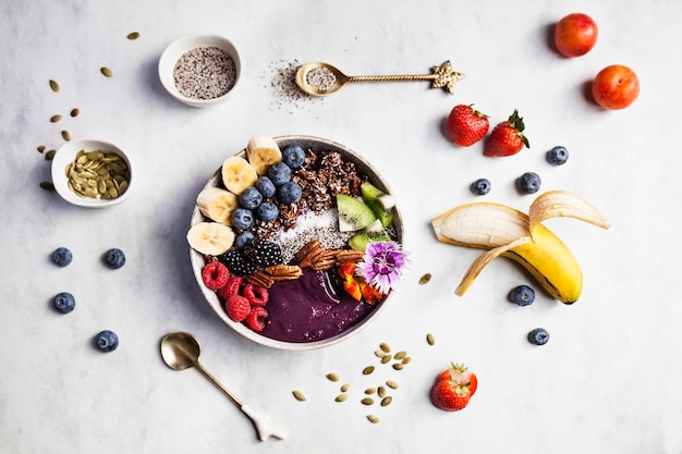 Bol d'açaï aux fruits frais pour le petit-déjeuner avec des myrtilles à la banane, des mûres, des fraises, des noix et des graines de kiwi