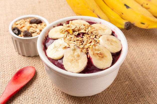 Photo bol d'açai avec banane et céréales sur toile de jute.