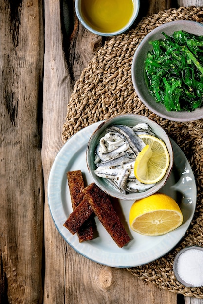 Bol d'anchois marinés ou filet de sardines à l'huile, servi avec citron, huile d'olive, sel et pain de seigle grillé