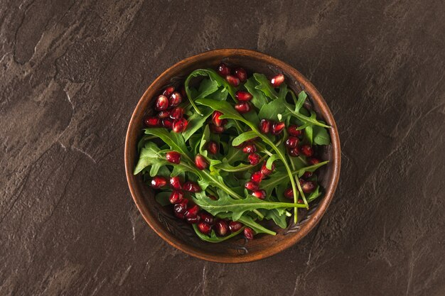 Bol en argile avec graines de grenade et roquette sur une table en pierre. Salade végétarienne diététique. Mise à plat.