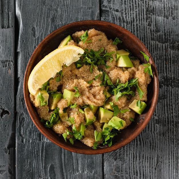 Bol en argile avec salade de graines d'amarante avec avocat, citron et persil sur une table rustique