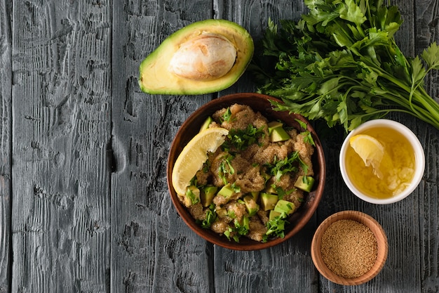 Bol en argile avec salade de graines d'amarante à l'avocat, citron, tomates et persil et bol à l'amarante sur une table rustique