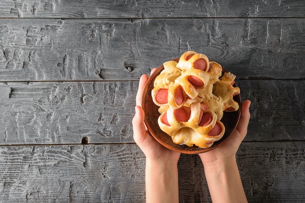 Bol en argile avec des saucisses dans la pâte dans les mains d&#39;un enfant sur une table en bois.