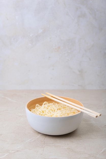 Bol en bambou blanc avec nouilles aux oeufs et baguettes sur fond clair