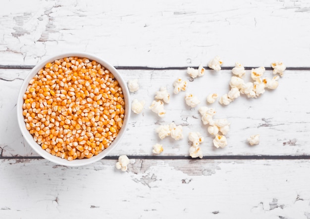 Bol blanc avec du maïs sucré cru et du pop-corn sur fond de bois