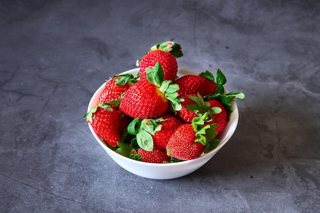 Un bol blanc avec des fraises sur un fond d'ardoise noire