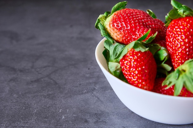 Un bol blanc avec des fraises sur un fond d'ardoise noire