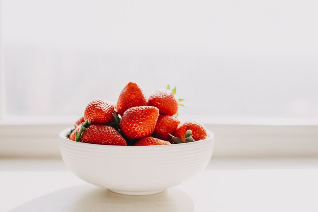 Bol blanc de fraises fraîches biologiques par la fenêtre