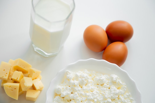 Un bol blanc avec des œufs de fromage cottage en dés de fromage et un verre de lait sur fond blanc...