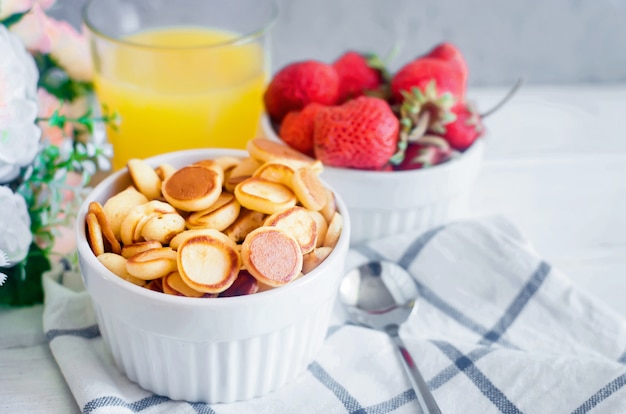 Bol blanc avec une petite crêpe aux céréales avec des fraises et un verre de jus d'orange.