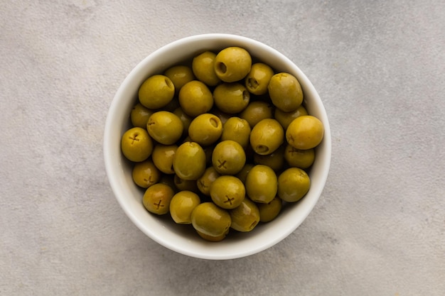 Bol blanc rempli d'olives vertes juteuses sur fond clair