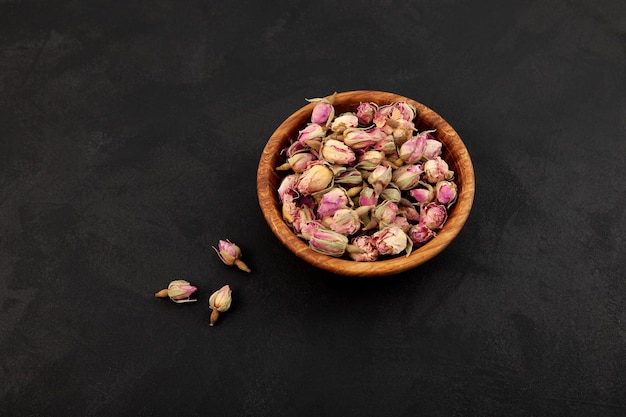 Bol en bois avec des boutons de roses roses séchées sur fond sombre Ingrédient pour une tisane saine