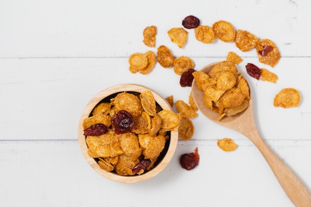 Le bol en bois de cornflakes au caramel aux raisins secs sur fond blanc pour une alimentation saine et un concept de petit-déjeuner