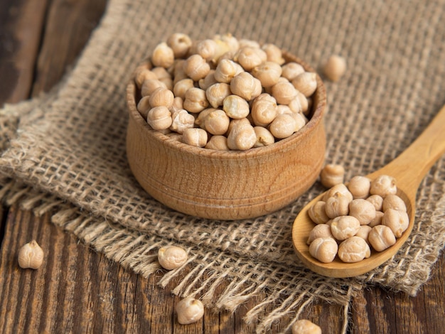 Bol en bois et cuillère en bois pleine de pois chiches sur un fond en bois