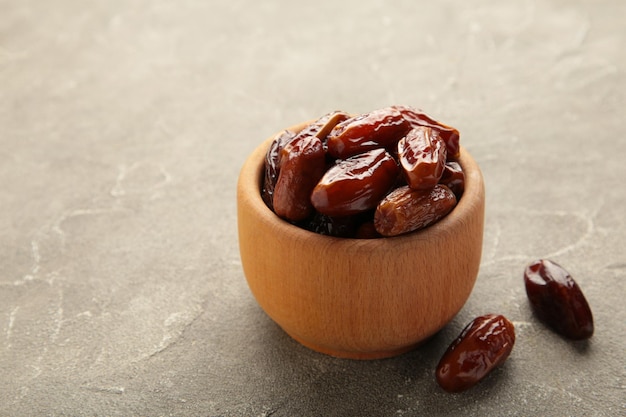 Bol en bois de dattes séchées sur fond de bois gris. Branche avec dates sur gris.