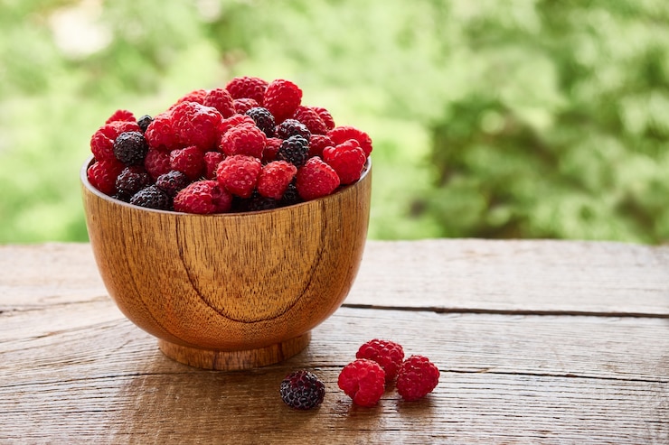 Photo bol en bois de délicieuses framboises rouges et noires sur fond de feuillage vert