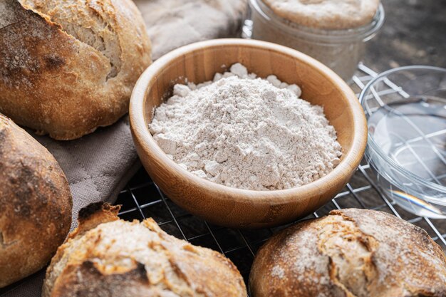 Bol en bois de farine de blé entier au milieu de petits pains au levain fraîchement cuits.