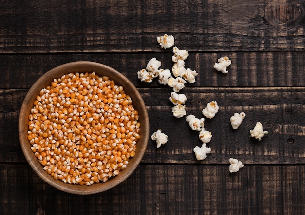 Bol en bois avec maïs sucré cru et pop-corn sur fond de bois