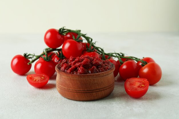 Bol en bois avec pâte de tomates et tomates sur table texturée blanche