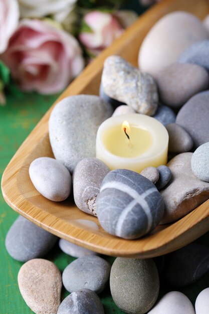 Bol en bois avec des pierres de spa et des bougies sur une table en bois sur fond de fleurs