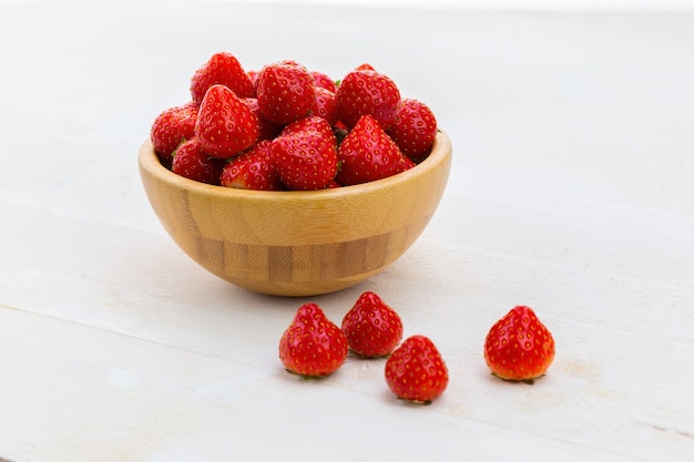 Bol en bois plein de fraises fraîches sur table blanche