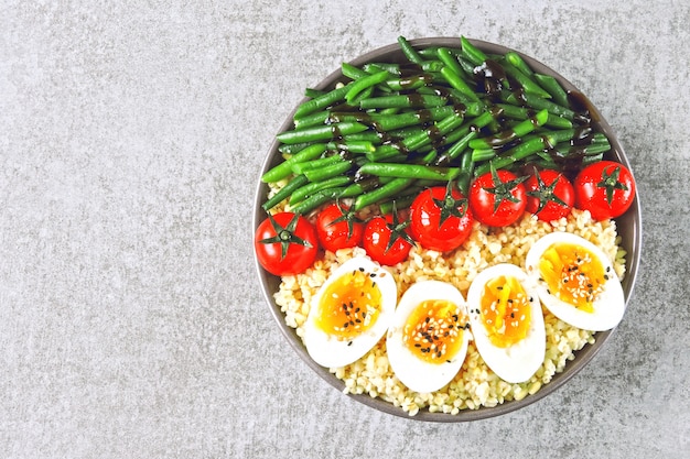 Bol de Bouddha avec boulgour, haricots verts, tomates cerises et moitiés d'oeufs durs. Des aliments sains dans un bol. Le concept de nutrition diététique.