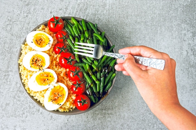 Bol de Bouddha avec boulgour, haricots verts, tomates cerises et moitiés d'oeufs durs. Des aliments sains dans un bol. Le concept de nutrition diététique.