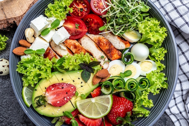 Bol de bouddha avec filet de poulet, quinoa, avocat, avocat, fromage feta, œufs de caille, fraises, noix et laitue. Concept de bol de désintoxication et de superaliments sains. Fond de recette de nourriture.