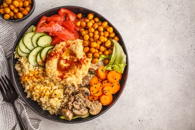 Bol de Bouddha avec légumes, champignons, bulgur, houmous et pois chiches cuits au four. Fond blanc, vue de dessus.