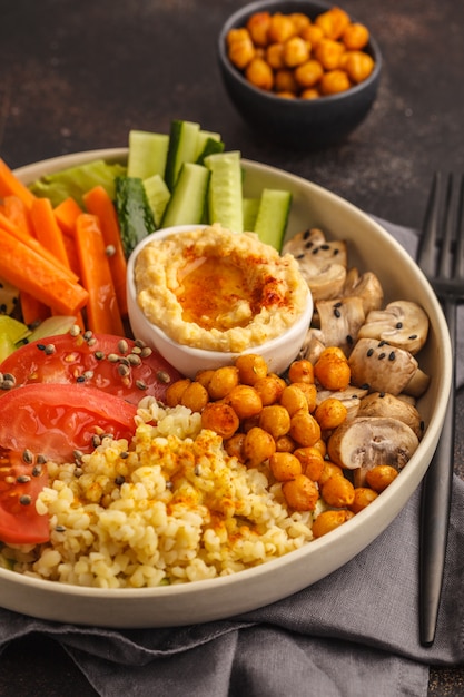 Bol de Bouddha avec légumes, champignons, bulgur, houmous et pois chiches cuits au four. Fond sombre.