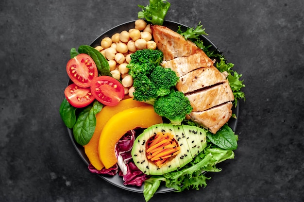 Bol de Bouddha. poulet, brocoli, pois chiches, citrouille, avocat, carotte, tomate, laitue sur une assiette avec couteau et fourchette